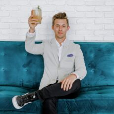 man in gray blazer raising drinking glass while sitting on sofa