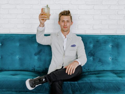 man in gray blazer raising drinking glass while sitting on sofa