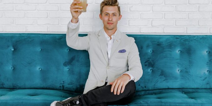 man in gray blazer raising drinking glass while sitting on sofa